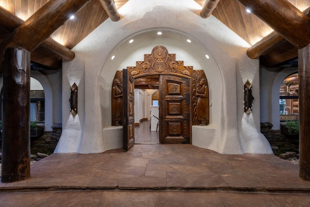 hall featuring beam ceiling, high vaulted ceiling, arched walkways, and stone tile flooring