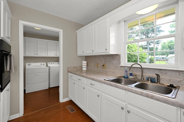  - kitchen featuring washing machine and clothes dryer, a sink, dark wood finished floors, white cabinetry, and light countertops