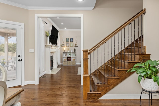 foyer with a fireplace with flush hearth, ornamental molding, wood-type flooring, baseboards, and stairs