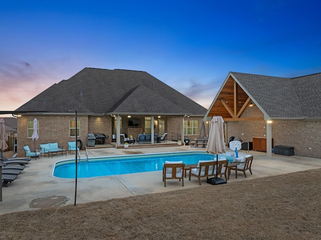 pool at dusk with an outdoor pool and a patio area