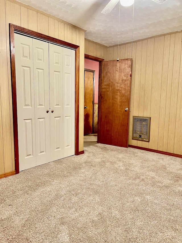 unfurnished bedroom with a ceiling fan, heating unit, carpet floors, wood walls, and a closet