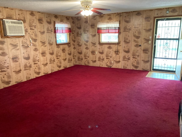 carpeted spare room featuring wood walls, a wall unit AC, ceiling fan, and a textured ceiling