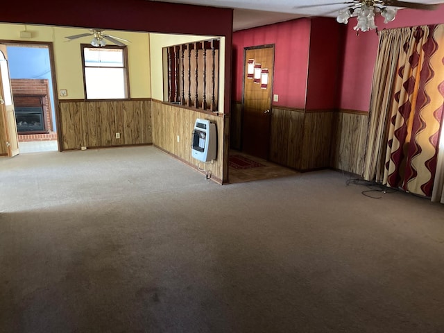 unfurnished room with heating unit, wood walls, a wainscoted wall, ceiling fan, and carpet flooring