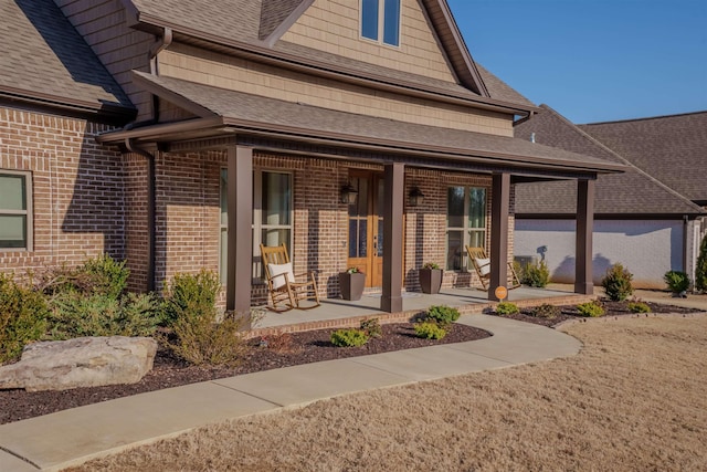 entrance to property with brick siding, a porch, and a shingled roof