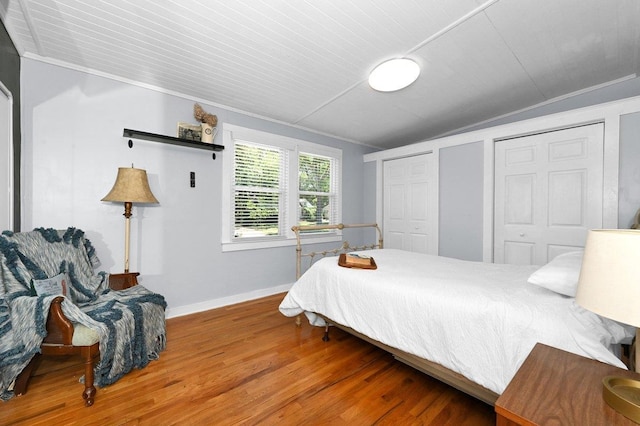 bedroom featuring wood-type flooring, multiple closets, ornamental molding, and wood ceiling