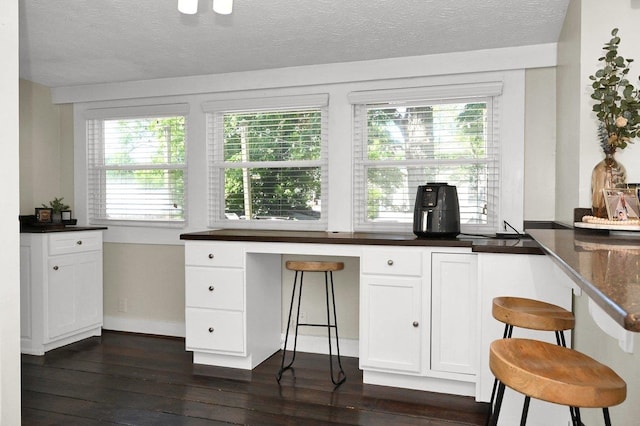 kitchen featuring a kitchen bar, white cabinetry, dark hardwood / wood-style flooring, and a textured ceiling