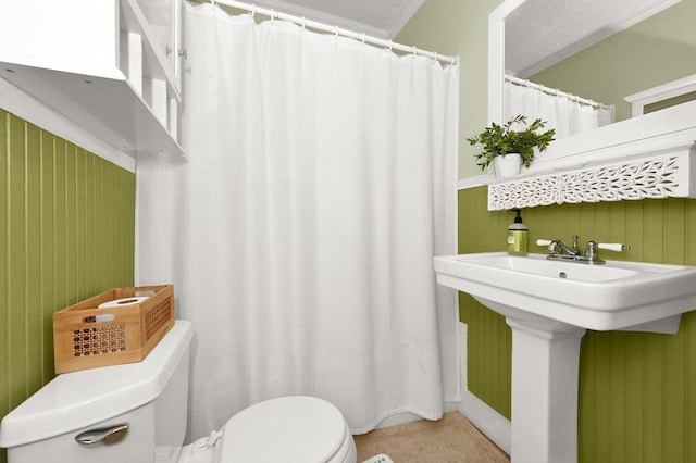 bathroom featuring a textured ceiling, wooden walls, toilet, and crown molding