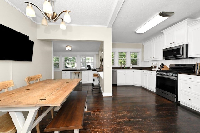 kitchen with a kitchen bar, white cabinetry, stainless steel appliances, and a textured ceiling