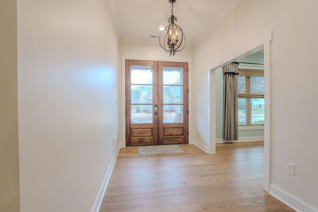 entryway featuring crown molding, an inviting chandelier, a wealth of natural light, and light hardwood / wood-style flooring