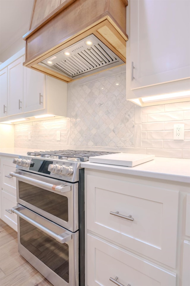 kitchen with white cabinets, tasteful backsplash, range with two ovens, and premium range hood