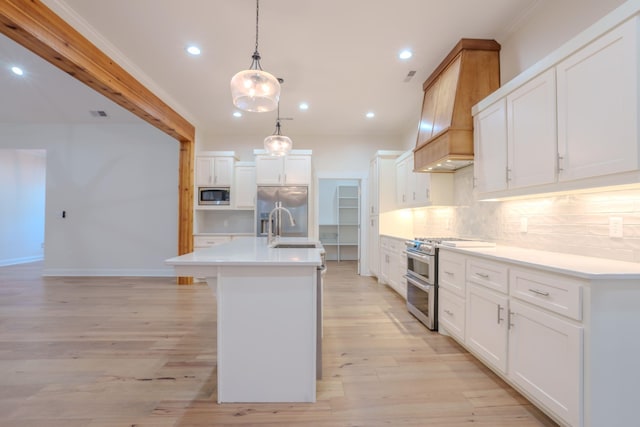 kitchen featuring tasteful backsplash, hanging light fixtures, stainless steel appliances, an island with sink, and white cabinetry