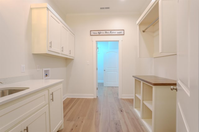 laundry room featuring cabinets, hookup for a washing machine, light hardwood / wood-style floors, sink, and ornamental molding