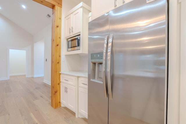 kitchen with light wood-type flooring, appliances with stainless steel finishes, white cabinets, and vaulted ceiling