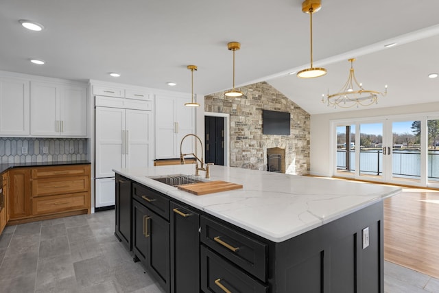 kitchen with a sink, white cabinets, open floor plan, light stone countertops, and pendant lighting