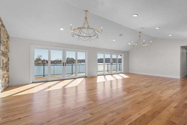 unfurnished living room with a water view, vaulted ceiling, french doors, light wood-style floors, and a chandelier