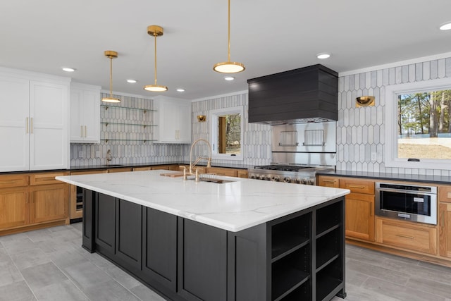 kitchen with a kitchen island with sink, custom range hood, a sink, and open shelves