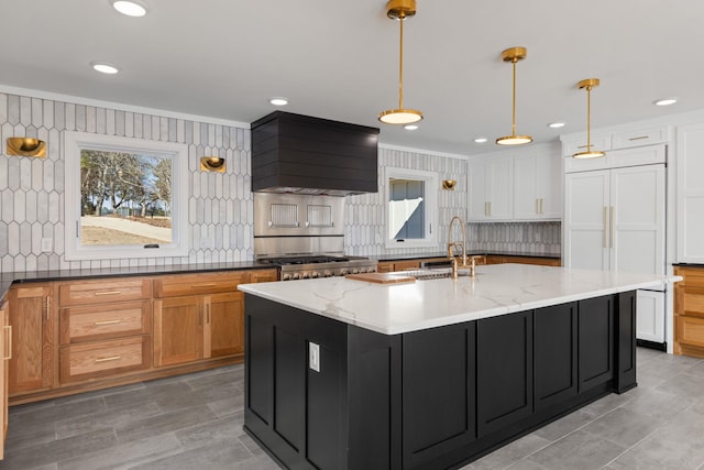 kitchen featuring decorative light fixtures, a center island with sink, premium range hood, and light stone countertops