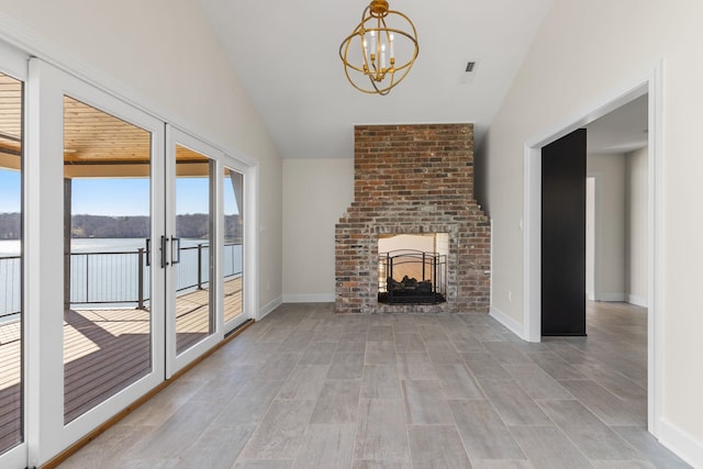 unfurnished living room featuring baseboards, a water view, french doors, a fireplace, and a notable chandelier