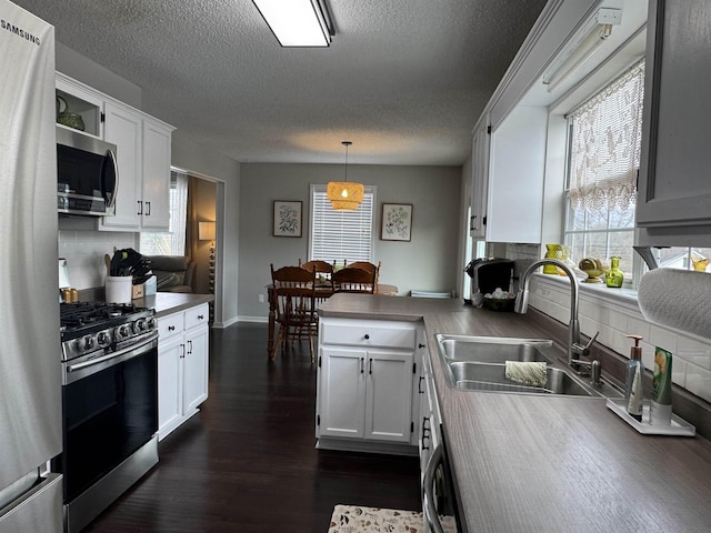 kitchen with kitchen peninsula, stainless steel appliances, sink, decorative light fixtures, and white cabinets