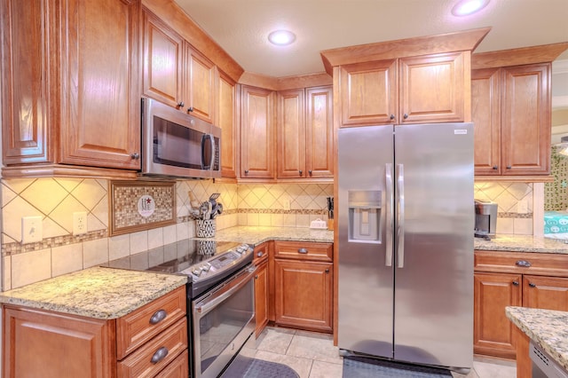 kitchen featuring tasteful backsplash, light tile patterned floors, light stone countertops, and appliances with stainless steel finishes