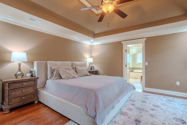 bedroom with crown molding, wood-type flooring, ensuite bathroom, and a raised ceiling