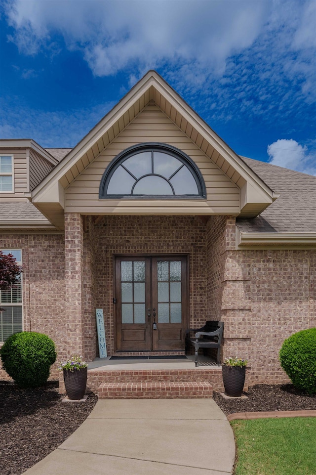  - property entrance featuring french doors, brick siding, and a shingled roof