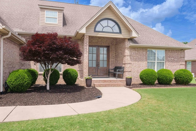  - property entrance with french doors, brick siding, a shingled roof, and a yard