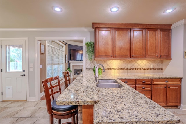 kitchen with a kitchen bar, sink, crown molding, kitchen peninsula, and light stone countertops