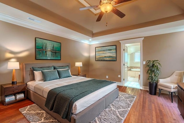  - bedroom with a tray ceiling, hardwood / wood-style flooring, ornamental molding, ensuite bath, and a ceiling fan