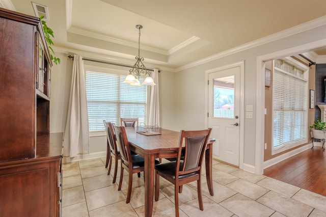 tiled dining area featuring a notable chandelier, ornamental molding, and a raised ceiling