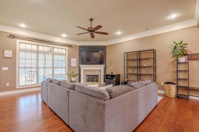 living room with crown molding, hardwood / wood-style flooring, a tile fireplace, and ceiling fan