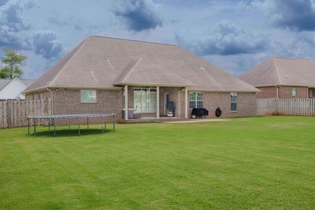  - back of property featuring a trampoline, brick siding, a patio, a fenced backyard, and roof with shingles