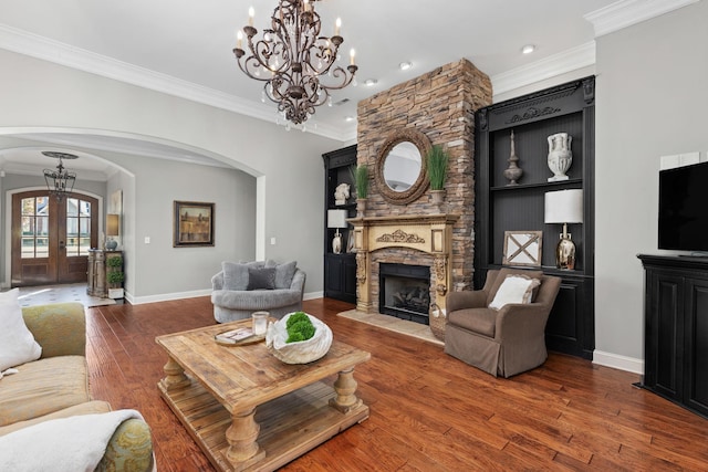 living room featuring french doors, a stone fireplace, hardwood / wood-style flooring, ornamental molding, and a notable chandelier