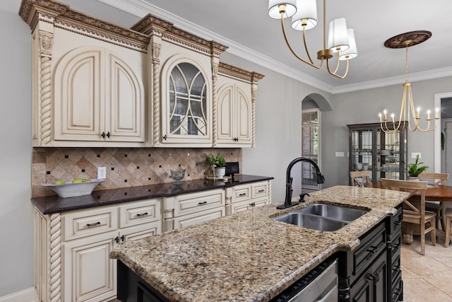 kitchen with sink, dark stone counters, a center island with sink, and an inviting chandelier