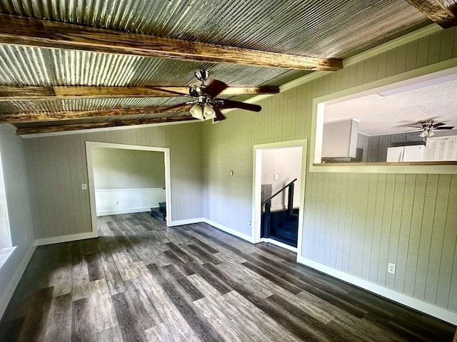  - unfurnished living room featuring a ceiling fan, dark wood-style flooring, wood walls, beam ceiling, and baseboards