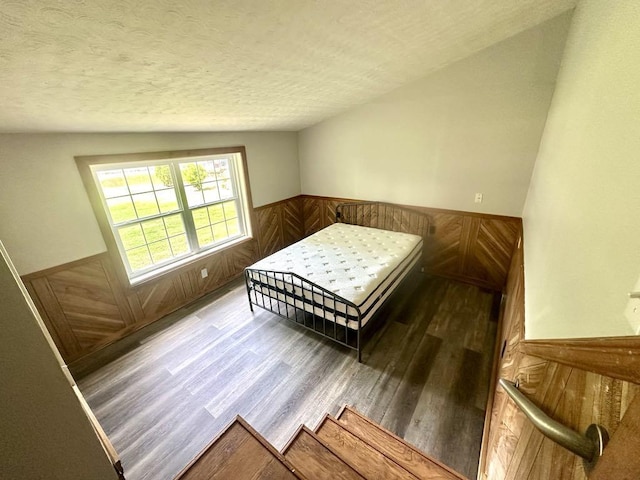  - bedroom with wainscoting, wood finished floors, wooden walls, and a textured ceiling