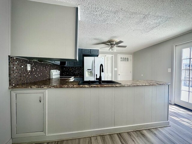  - kitchen with light wood-style floors, a sink, a peninsula, electric range, and dark stone counters
