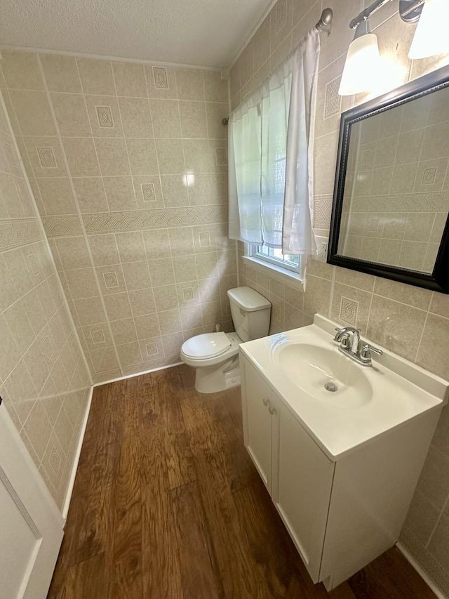  - half bath with tile walls, wood finished floors, toilet, vanity, and a textured ceiling