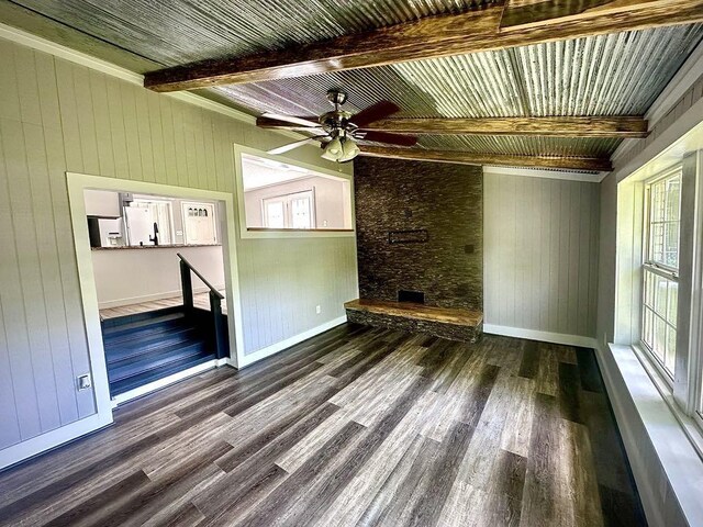  - unfurnished living room with beam ceiling, wood finished floors, baseboards, ceiling fan, and wood walls