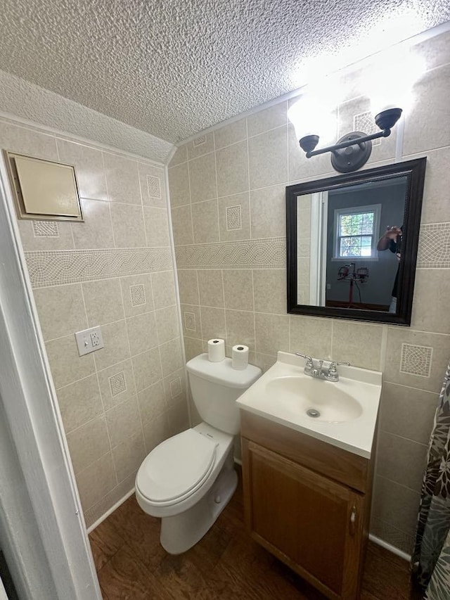  - bathroom with a textured ceiling, tile walls, vanity, toilet, and wood finished floors
