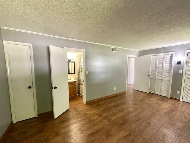  - unfurnished bedroom featuring a textured ceiling, wood finished floors, ensuite bathroom, ornamental molding, and two closets