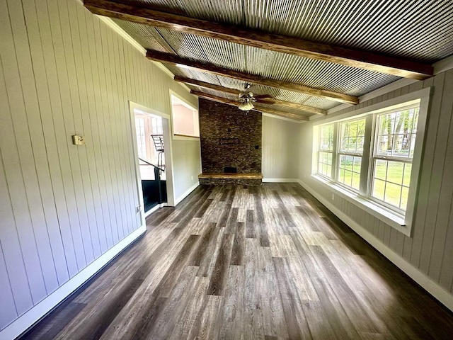  - unfurnished living room featuring beam ceiling, dark wood finished floors, a fireplace, wooden walls, and a ceiling fan