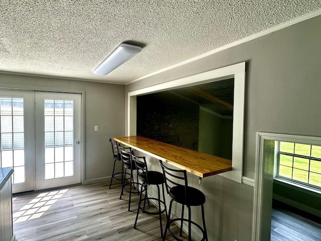  - kitchen featuring a textured ceiling, butcher block countertops, wood finished floors, ornamental molding, and a breakfast bar area