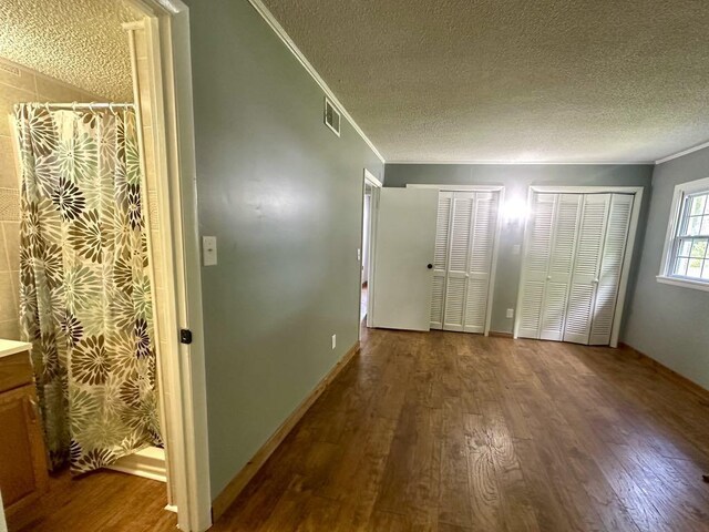  - unfurnished bedroom featuring crown molding, a textured ceiling, wood finished floors, and two closets