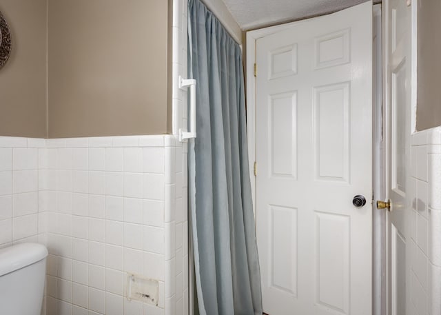 bathroom featuring a textured ceiling, toilet, and tile walls