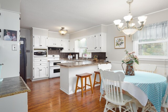 kitchen with backsplash, kitchen peninsula, a chandelier, white appliances, and white cabinets