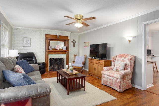 living room with ceiling fan, light hardwood / wood-style floors, crown molding, and a brick fireplace