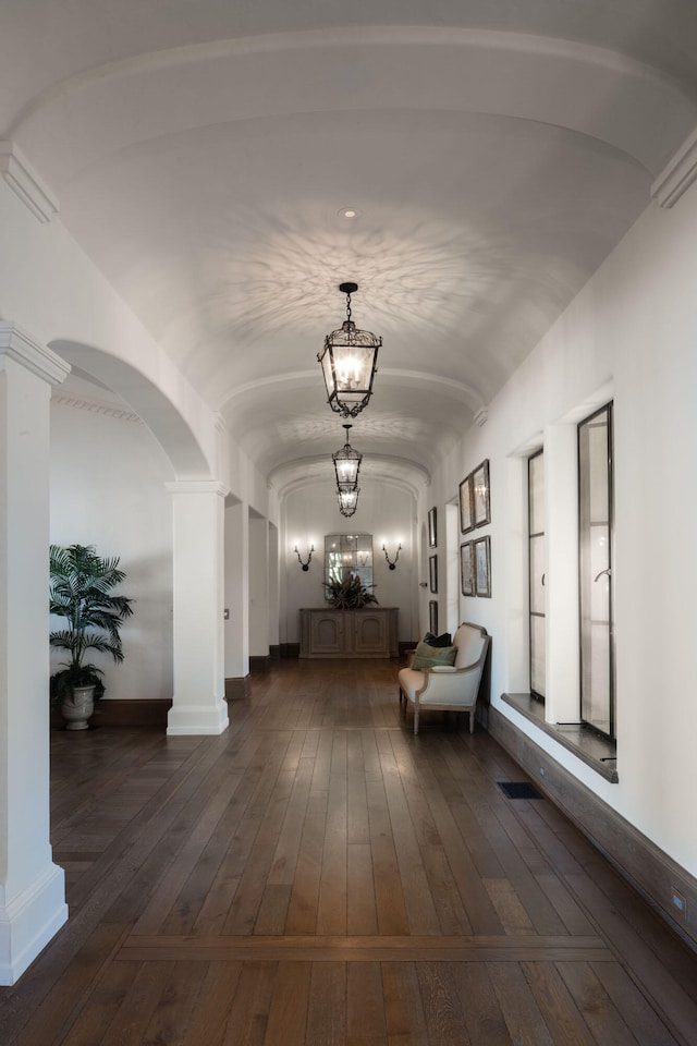 corridor featuring a notable chandelier, dark hardwood / wood-style floors, and ornate columns