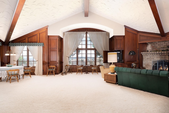 living room featuring a fireplace, vaulted ceiling with beams, brick wall, and carpet flooring