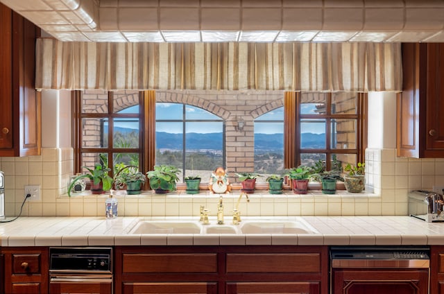 kitchen featuring backsplash, dishwasher, a mountain view, sink, and tile counters